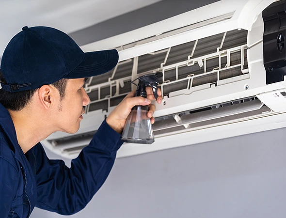 Technician cleaning AC unit with spray bottle during comprehensive HVAC maintenance for optimal performance.