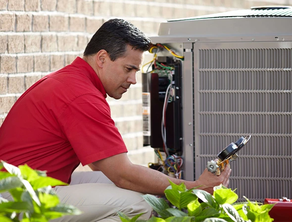 Red shirt technician testing HVAC unit with gauge during professional heat pump installation service.