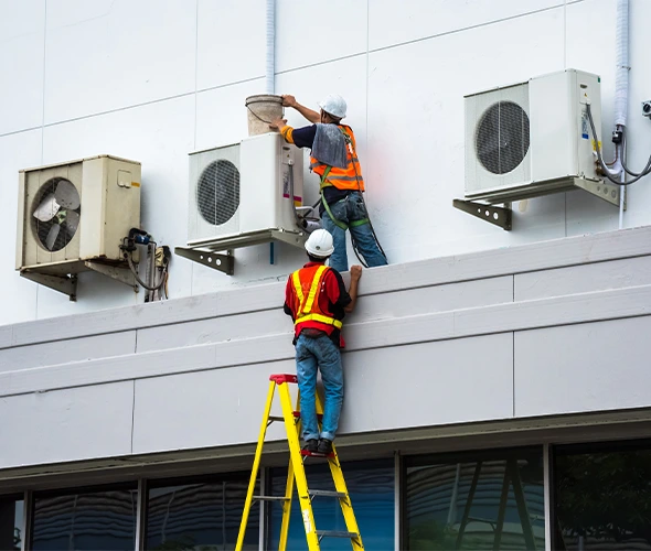 Two technicians on ladders servicing wall-mounted HVAC units during professional HVAC repair and maintenance work.